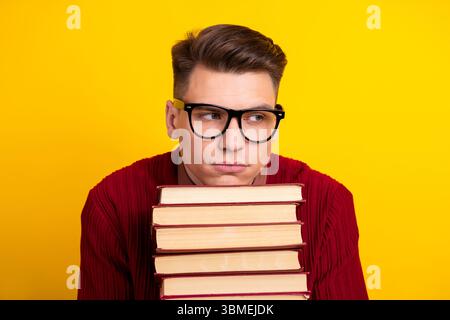 Gutaussehender junger männlicher Student, der Buch mit nachdenklichem Ausdruck auf gelbem Hintergrund hält Stockfoto