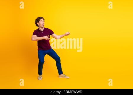 Fröhlicher junger Mann in lässiger Kleidung, der mit Aufregung auf einem leuchtend gelben Hintergrund Gesten zeigt, die lebendige Energie zeigen. Stockfoto