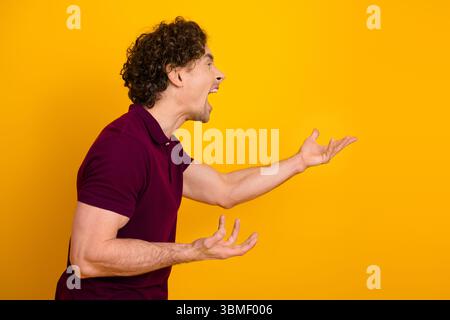 Ausdrucksstarker junger Mann, der leidenschaftlich auf einem leuchtend gelben Hintergrund in lässiger Kleidung mit Emotionen und Stil blickt Stockfoto