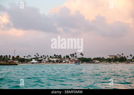 Die Wellen schlagen sanft gegen das Ufer, während Palmen in der Nähe von lebhaften Booten und Geschäften in einer Küstenstadt schweben. Stockfoto