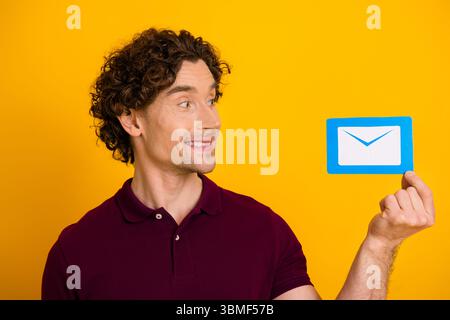 Junger Mann in lässiger Kleidung mit einem Umschlag-Symbol vor leuchtendem gelbem Hintergrund, der Kommunikation zum Ausdruck bringt Stockfoto