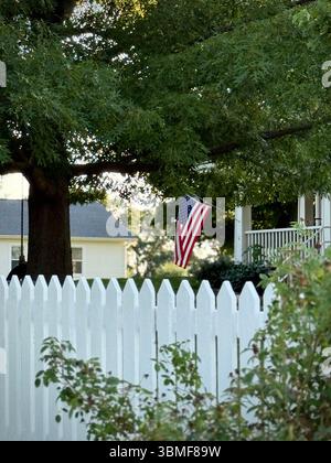 Eine amerikanische Flagge an einem weißen Streifenzaun, der im Sommer von einer Veranda hängt Stockfoto