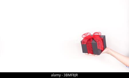 Eine stilvolle schwarze Geschenkbox mit einem leuchtend roten Band und einer Schleife, isoliert auf weißem Hintergrund, perfekt für verschiedene Anlässe und ideal für den Markt Stockfoto