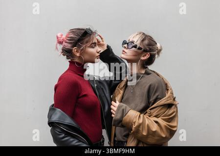 Stilvolle Schöne Junge Teenager Frau Freundin In Modischer Kleidung Mit Brille, Lederverdrehungen Und Pullover Stehen Und Posieren In Der Nähe Der Grauen Mauer In Der Stadt Stockfoto