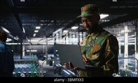 Spezialist für Informationstechnologie der Armee für die Fehlersuche in Rechenzentren bei militärischen Computersystemen und Netzwerken mit Laptops. Soldat im Serverraum der Kommandozentrale mit Notebook, Stockfoto