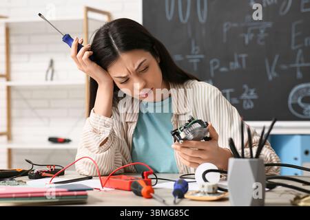 Verärgerte Erfinderin mit Schraubendreher und Computerlüfter am Tisch in der Werkstatt Stockfoto