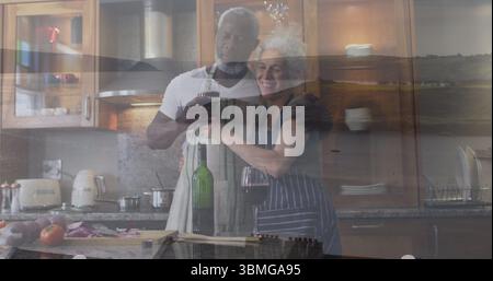 Toastpaare mit Schürzen, die in der Küche kochen, mit Weingläsern, Schneidebrett, Messer Stockfoto