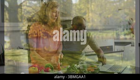 Paare, die rote Paprika und Gemüse an Bord in der Küche schneiden, Rezept auf Laptop ansehen Stockfoto