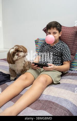 12-jähriger Teenager neben seinem Hund und mit einem Stück Kaugummi im Mund vertikal. Stockfoto