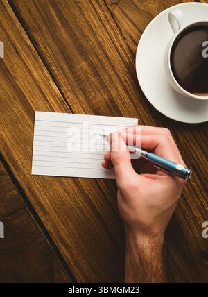 Abgeschnittene Handschrift auf Papier am Schreibtisch mit Kaffeetasse Stockfoto