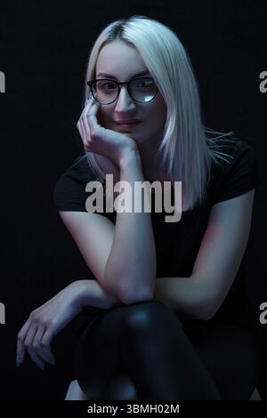 Nachdenkliche junge kaukasische schöne blonde Frau mit Brille. Nahaufnahme Porträt im Neonlicht Stockfoto