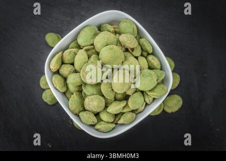 Teil der Wasabi-beschichteten Erdnüsse auf einer rustikalen Schieferplatte (selektiver Fokus, Nahaufnahme) Stockfoto