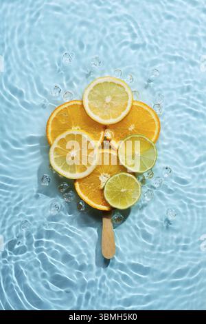 Kreative Eislolly aus Zitrusfrüchtescheiben auf blauem Wasserhintergrund mit konzentrischen Kreisen und Kräuseln. Erfrischendes Dessertkonzept für den Sommer Stockfoto