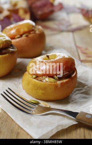 Hausgemachte, im Ofen gebackene Äpfel, gefüllt mit Hüttenkäse, Kürbiskernen und Mandeln auf Backpapier. Gefallene Blätter als Herbstdekor Stockfoto