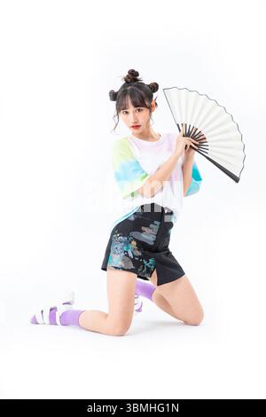 Eine schöne junge Studentin in einem kurzen Rock im chinesischen Stil hält ein traditionelles chinesisches Papier fan​ Stockfoto