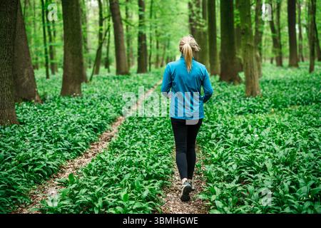 Frau, die auf dem Waldweg läuft. Läuferin in Sportbekleidung. Freizeitaktivitäten im Freien Stockfoto