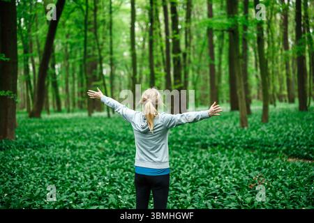 Sportlerin feiert Freiheit mit weit offenen Armen in der Natur, Symbol für Entspannung und geistiges Wohlbefinden. Baden im Wald Stockfoto