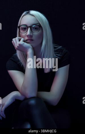 Nachdenkliche junge kaukasische schöne blonde Frau mit Brille. Nahaufnahme Porträt im Neonlicht Stockfoto