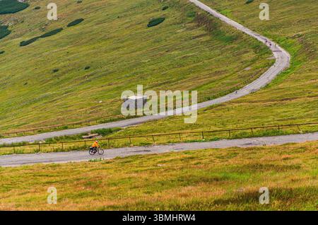 Ein Mann fährt auf einer Feldstraße mit dem Fahrrad. Die Straße ist von einem grasbewachsenen Hügel umgeben Stockfoto