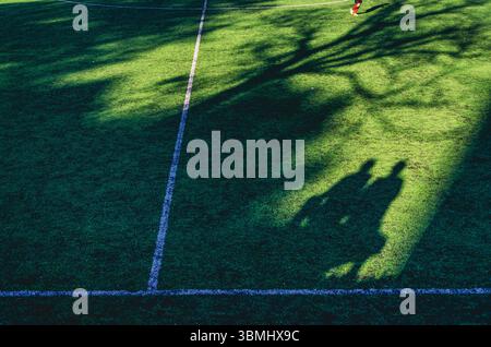 Ein Fußballfeld mit einem Schatten von zwei Menschen auf dem Gras. Der Schatten ist auf dem Gras und die Menschen sind nicht sichtbar Stockfoto