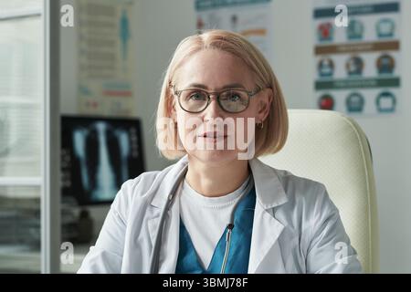 Porträt einer Kaukasierin mittleren Alters mit Brille in Arztpraxis mit Blick auf die Kamera während der Konsultation mit Diabe Stockfoto