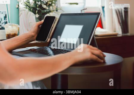Geschäftsfrau benutzt Handy, während sie am Laptop arbeitet. Stockfoto