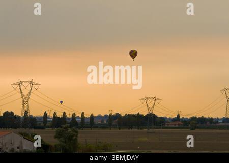 Heißluftballons gleiten bei einem ruhigen Sonnenuntergang über Felder Stockfoto