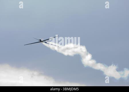 Kleines Flugzeug, das Kunstflugmanöver durchführt und eine weiße Rauchspur gegen einen blauen Himmel hinterlässt Stockfoto