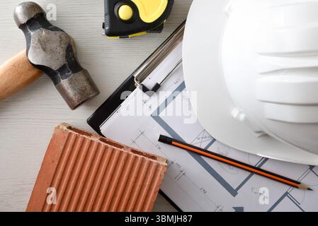 Konzeptioneller Hintergrund von Baumaterialien und Werkzeugen wie Helm, Ziegel, Hammer, Meterstab und Blaupausen. Draufsicht. Stockfoto