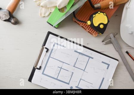 Allgemeine Ansicht des Schreibtischs des Architekten mit Mappe mit Plänen mit Notizen für ein Bauprojekt und umliegenden Elementen. Draufsicht. Stockfoto