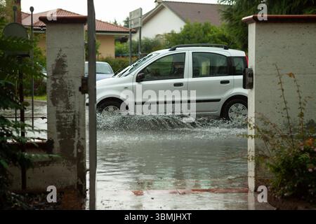 Weißes Auto, das nach starkem Regen in Wohngebieten auf überfluteten Straßen spritzt Stockfoto