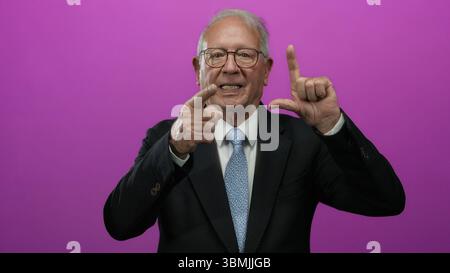Senior Mann im Business-Anzug Gesten vor isoliertem rosa Hintergrund, der Konzept und Emotionen in ausdrucksstarken Posen ausdrückt. Stockfoto
