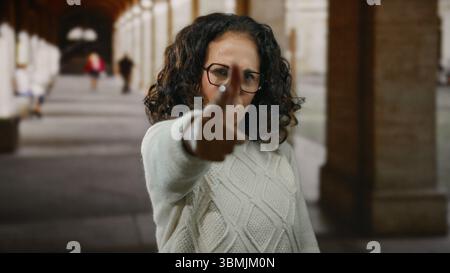 Frau mit lockigen Haaren, die tagsüber mit dem Finger auf spielerische Weise außerhalb des Gehweges des Universitätsgeländes gestickt hat Stockfoto
