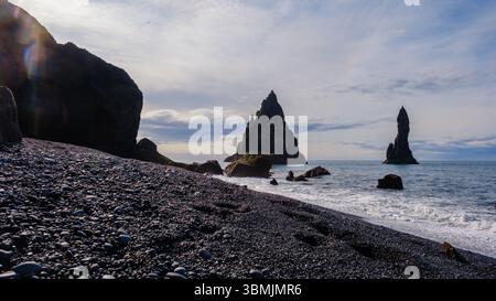 Wellen schlagen sanft gegen den dramatischen schwarzen Sand des Reynisfjara Beach in Island, mit majestätischen Basaltfelsen, die majestätisch aus dem Meer ragen. Stockfoto