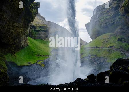 Der Kvernufoss Wasserfall bietet spektakuläre Wasserfedern, die von felsigen Klippen strömen, umgeben von üppigem Grün und landschaftlich reizvollen Landschaften Islands. Besucher bewundern die atemberaubende natürliche Schönheit. Stockfoto