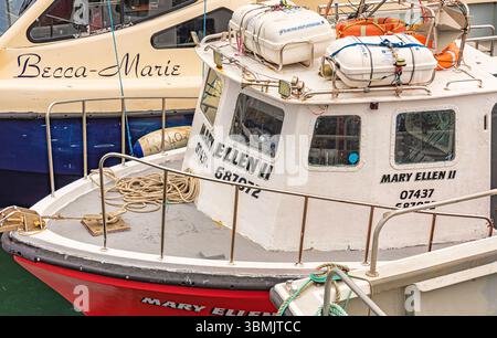 Ein kleines Boot liegt an einem anderen in einem Hafen. Das Seil wird auf dem Deck aufgewickelt und Rettungsflöße und Rettungsgürtel befinden sich auf dem Dach des Radhauses. Stockfoto