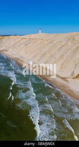 Entdecken Sie die atemberaubenden Sandklippen entlang der Küste des Rubjerg Knude Leuchtturms Nordjütland Dänemark, wo Wellen unter einem klaren blauen Himmel gegen die Küste krachen. Stockfoto