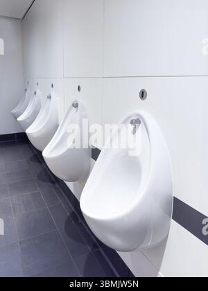 Eine Reihe weißer Keramik-Urinale an der Wand einer sauberen und modernen öffentlichen Toilette mit Fliesenboden Stockfoto