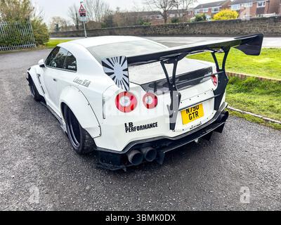 White Works nissan GTR Sportwagen mit schwarzer Kapuze auf einer nassen Straße, individuellem Karosseriekit und eleganten Designelementen Stockfoto