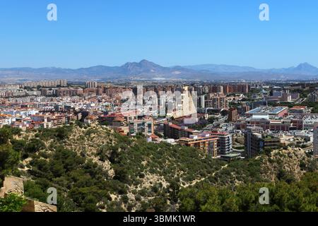 Panoramablick auf die Stadt Alicante mit Stierkampfarena, städtischen Gebäuden und Bergen im Hintergrund unter klarem Himmel. Stockfoto