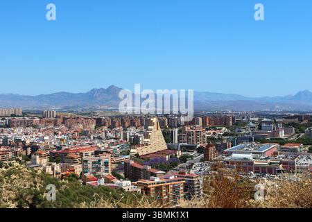 Panoramablick auf die Stadt Alicante mit Stierkampfarena, städtischen Gebäuden und Bergen im Hintergrund unter klarem Himmel. Stockfoto