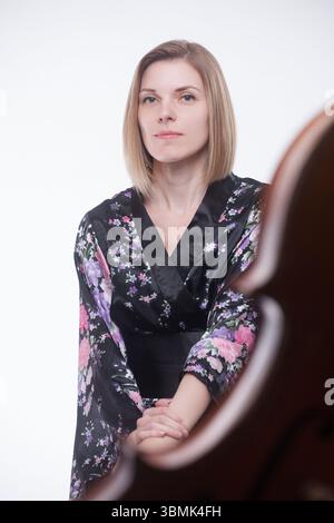 Weiße Frau, 30er Jahre, im Studio mit Cello. In schwarzem Blumengewand, mit gefalteten Händen. Stockfoto