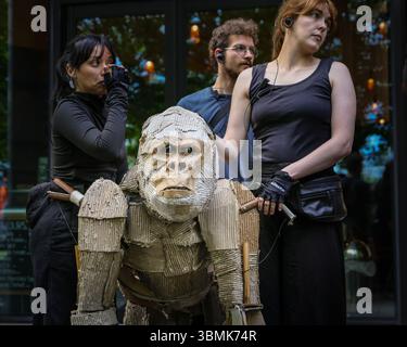 London, Großbritannien. Juni 2025. Die Darsteller laufen vom Bridge Theatre zur Themse mit der Tower Bridge dahinter. DIE HERDEN sind öffentliche Kunst und Klimaschutz. Von April bis August 2025 fahren lebensgroße Puppentiere auf einer 000 km langen Route vom Kongo-Becken zum Polarkreis, was ihren Flug vor der Klimakatastrophe symbolisiert und in vielen Städten und Ländern hält. Quelle: Imageplotter/Alamy Live News Stockfoto