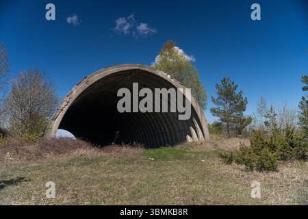 Verlassener Betonflugzeughangar aus der Sowjetzeit im ländlichen Estland, blauer Himmel, postmilitärische Architektur, städtische Erkundung. Stockfoto