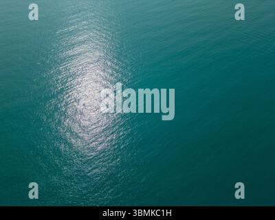 Aus der Vogelperspektive auf das ruhige türkisfarbene Meer mit schimmernden Sonnenlichtreflexionen auf der Oberfläche. Friedlicher und abstrakter natürlicher Hintergrund Stockfoto