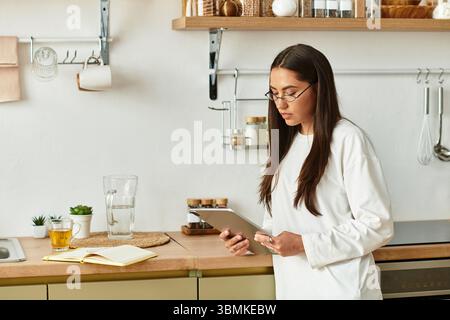 Eine junge Frau in bequemer Kleidung genießt ihr Tablet in einer gemütlichen Küche. Stockfoto
