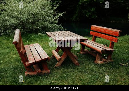 Blick aus der Nähe auf rustikale rot gestrichene Bänke und Tisch am Wasser auf einer grünen Wiese. Idealer Ort für ein ruhiges Mittagessen in der Natur. Krupajsko vrelo in Serbien Stockfoto