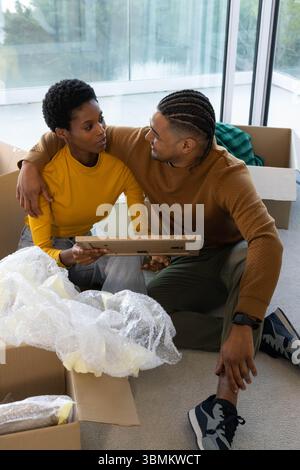 Auspacken diverser Paare, die einen Bilderrahmen auf Teppichboden im Wohnzimmer untersuchen, mit Umzugskartons Stockfoto