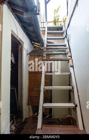 Holztreppe mit einem Bambusschirm davor. Die Treppe ist sehr schmal und hat viele Stufen Stockfoto