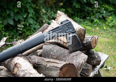 Outdoor-Szene mit einer Axt neben einem Holzhaufen, die auf rustikales Wohnen, Brennholzzubereitung oder Waldarbeiten hindeutet. Stockfoto